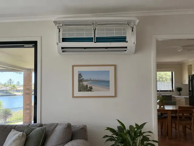 Open split system with clean filters on a lounge room wall, above a framed beach print, in Paradise Point