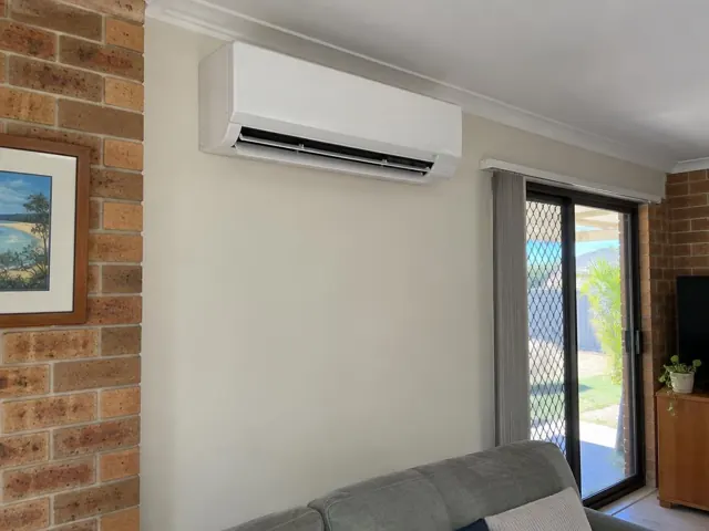 Clean split system indoor unit mounted high on a beige wall in a living room with brick feature wall in Biggera Waters