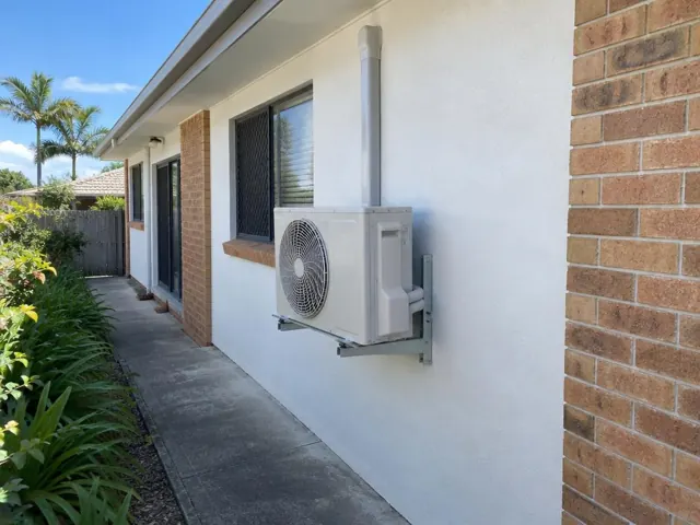 Wall-mounted air conditioner outdoor unit beside a brick-and-render house exterior in Coombabah