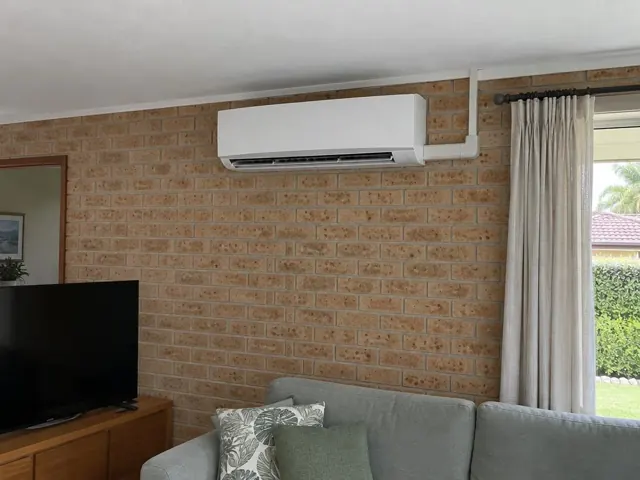 Wall-mounted split system on a brick living room wall beside curtains and a sofa in Labrador